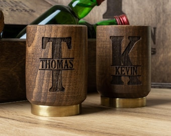 May include: Two wooden shot glasses with brass bases. The glasses are engraved with the letters "T" and "K" and the names "Thomas" and "Kevin".