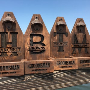 May include: Four wooden bottle openers with personalised names and the date "18 June 2019" engraved on each. The bottle openers are brown and have a metal bottle opener attached to the top.