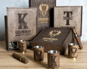 May include: Wooden boxes with personalised engravings for groomsmen, featuring names, initials, and the date "June 20, 2025". The boxes are accompanied by wooden shot glasses with matching engravings.