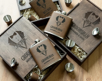 May include: Personalised brown leather hip flasks with stainless steel detailing, displayed in wooden boxes. Each flask is engraved with a name, title, and date. Includes shot glasses and a funnel.