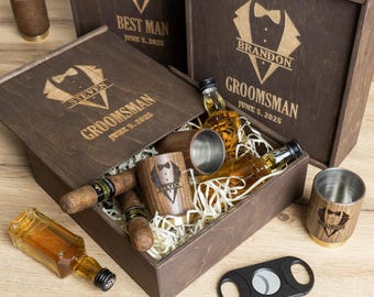May include: A wooden gift box with a personalised engraved design for a groomsman. The box includes a bottle of spirits, two shot glasses, two cigars and a cigar cutter. The box is decorated with wood shavings and has a brown finish.