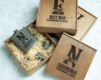May include: Wooden gift boxes with engraved text and a flask set. One box reads "EVAN BEST MAN OCTOBER 4, 2025". Another box reads "NICK GROOMSMAN OCTOBER 4, 2025". The flask is grey and has the letter "N" and the name "NICK" engraved on it.