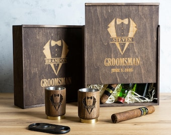 May include: Two wooden boxes with engraved tuxedo designs and the words "Groomsman" and the names "Brandon" and "Steven". The boxes contain shot glasses, a cigar, and bottles of spirits.