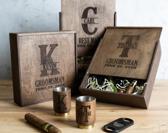 May include: Three wooden boxes with engraved initials and the words "Best Man", "Groomman" and "Groomman". The boxes are open and contain a bottle of wine, a cigar, and two shot glasses. The shot glasses are engraved with the initials "K" and "T".