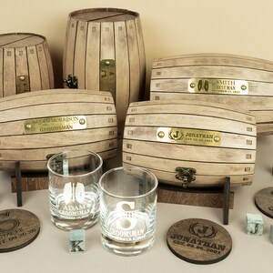 May include: Set of personalised wooden barrel boxes with engraved brass plates. Each box has a different name and date. The set also includes two engraved whisky glasses and coasters.