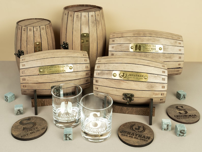 May include: Set of personalised wooden barrel boxes with engraved brass plates. Each box has a different name and date. The set also includes two engraved whisky glasses and coasters.