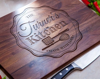 May include: A rectangular wooden cutting board with the text "The Turner's Kitchen" engraved in a decorative emblem. The board features a spatula and whisk design, with the words "Made with Love" below. A stainless steel knife rests on the side.