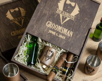 May include: A wooden box with a lid, filled with a small bottle, a wooden cup, and two cigars. The lid is engraved with the text "Groomsman" and "June 5, 2025".