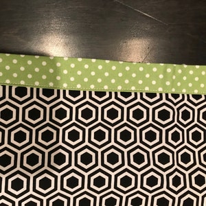 May include: A black and white fabric with a honeycomb pattern. The fabric has a green and white polka dot trim.