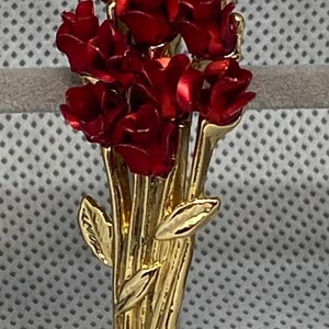 Può includere: Spilla in metallo dorato a forma di bouquet di fiori rossi. I fiori hanno una finitura lucida e anche gli steli e le foglie sono dorati. Una classica spilla floreale.