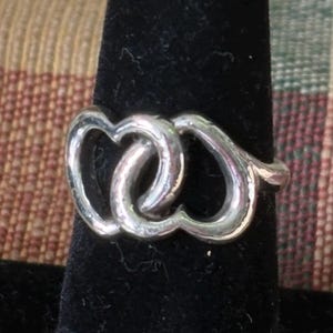 May include: A silver-toned ring featuring two interlocking heart-shaped outlines. The metal band is polished and smooth, forming a continuous design where the two open heart shapes are joined together in the center of the ring's face.