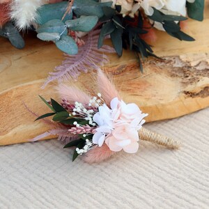 May include: A small bouquet of dried flowers in shades of pink and white, with sprigs of greenery. The bouquet is tied with twine and features a pink pampas grass plume.
