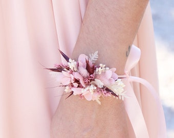 Puede incluir: Un brazalete de flores secas de color rosa y blanco con una cinta de satén rosa.