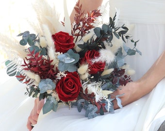 Puede incluir: Un ramo de novia con rosas rojas, hierba de la pampa seca y hojas de eucalipto.