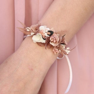 Könnte beinhalten: Ein zartes Blumenarmband mit einem weißen Band. Das Armband besteht aus kleinen, getrockneten Blumen in Braun-, Weiß- und Rosatönen.