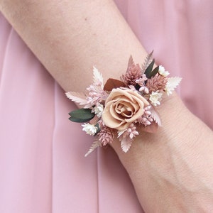 Könnte beinhalten: Ein Handgelenkscorsage mit einer einzelnen rosafarbenen Rose und getrockneten Blumen in Rosa- und Brauntönen.