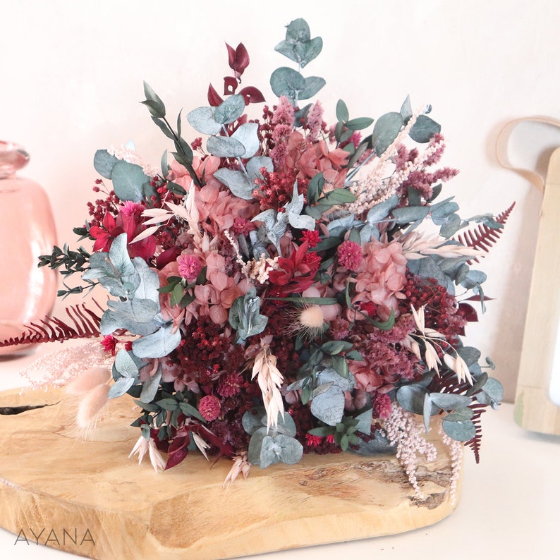 May include: A dried flower bouquet with pink, burgundy, and white flowers, and blue-green eucalyptus leaves.