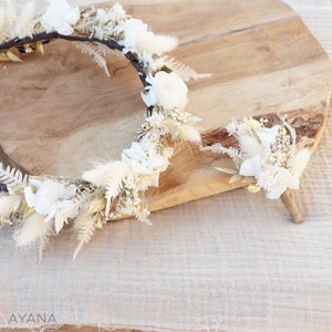 May include: A white and gold floral crown and matching buttonhole made with dried flowers and greenery. The crown is circular and the buttonhole is a small bouquet.