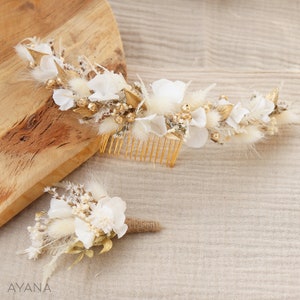 May include: A set of two white and gold floral hair accessories. The larger piece is a comb with dried flowers and feathers. The smaller piece is a boutonniere with dried flowers and a hessian ribbon.