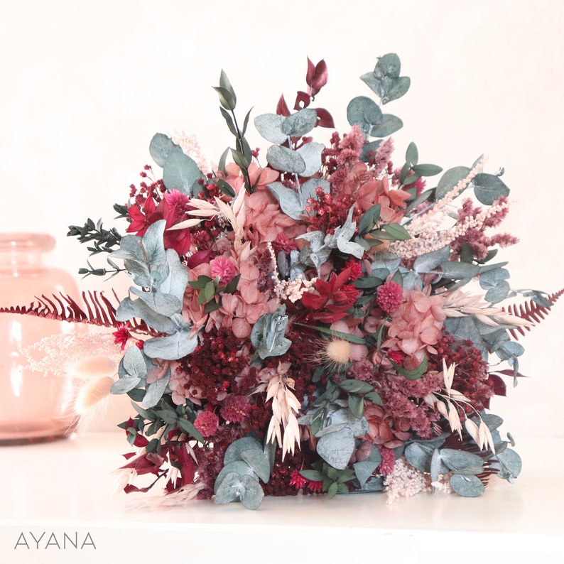 May include: A bouquet of dried flowers in shades of pink, red, and white. The bouquet includes eucalyptus, hydrangeas, and other dried flowers.