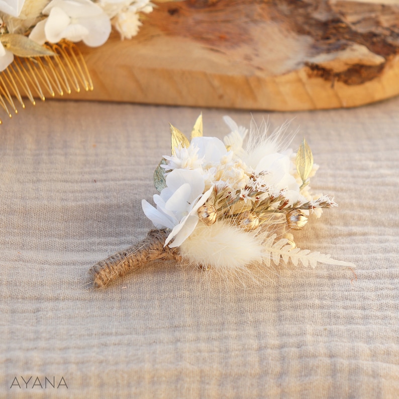 May include: A small white and gold floral bouquet featuring dried flowers, feathers, and gold accents. The bouquet is tied with twine and is ideal for a wedding or special occasion.
