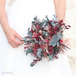 May include: A bouquet of dried flowers in shades of burgundy, pink, and green. The bouquet includes eucalyptus, ferns, and other dried flowers.