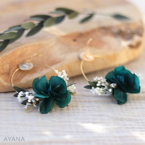 Op de afbeelding: Een paar gouden creolen met een turquoise bloem en witte gedroogde bloemen die aan elke creool zijn bevestigd.