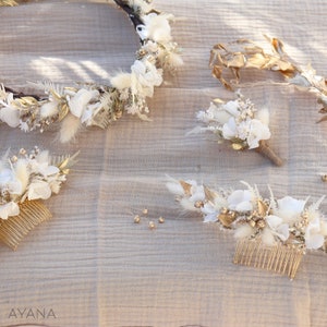 May include: A set of three white and gold floral hair combs. The combs are made with dried flowers, branches, and gold accents. The combs are arranged on a beige fabric background.