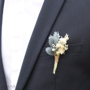 May include: A small bouquet of dried flowers in shades of blue and white, tied with twine, is pinned to a dark suit jacket.