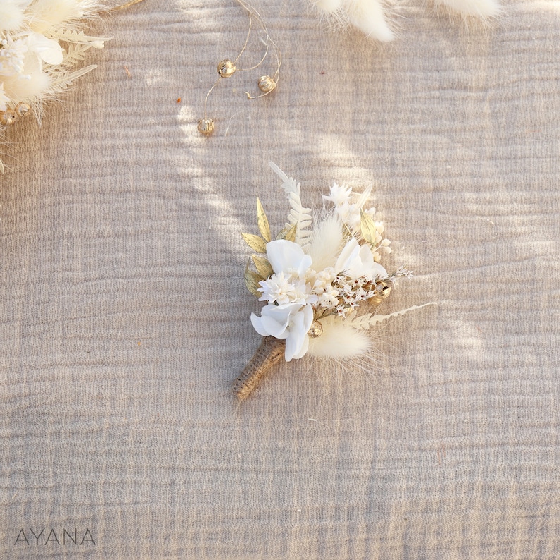 May include: A small bouquet of dried flowers in shades of white and gold, tied with twine. The bouquet includes white flowers, dried grasses, and gold accents.