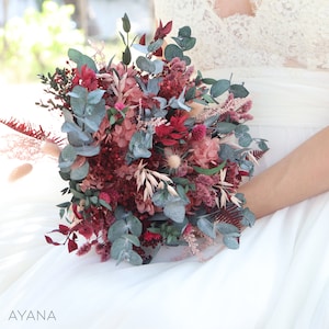 May include: A bridal bouquet with a mix of dried flowers and greenery in shades of burgundy, pink, and green. The bouquet features eucalyptus, dried hydrangeas, and other dried flowers.