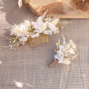May include: A set of two white and gold floral hair combs. The larger comb features a variety of dried flowers, including white hydrangeas, pampas grass, and gold-painted foliage. The smaller comb is a simple bouquet of white flowers and dried grasses.
