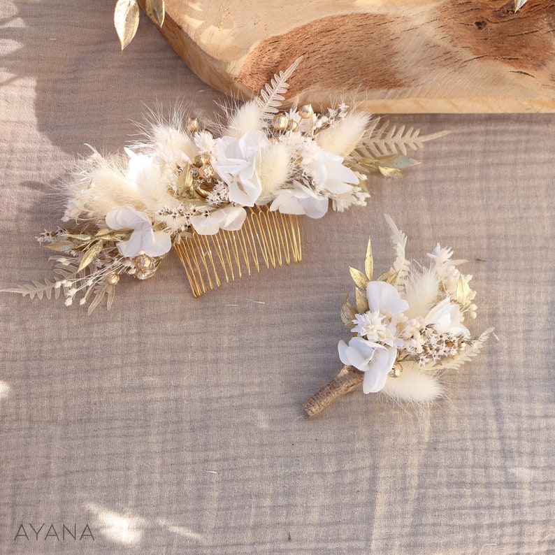 May include: A set of two white and gold floral hair combs. The larger comb features a variety of dried flowers, including white hydrangeas, pampas grass, and gold-painted foliage. The smaller comb is a simple bouquet of white flowers and dried grasses.