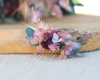Puede incluir: Un peine para el cabello floral con un peine plateado y flores secas en tonos de rosa, morado y blanco. Las flores están dispuestas en un racimo e incluyen hortensias, aliento de bebé y otras flores pequeñas.