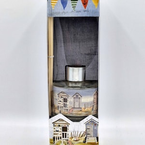 May include: A reed diffuser with a blue and white beach hut design. The box has the text "Wood Sage & Ocean Mist Fragranced Diffuser Diffuseur de Parfum" and colourful flags with an anchor.