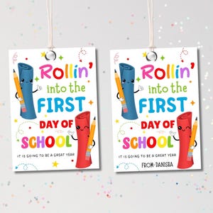 Könnte beinhalten: Zwei rechteckige Geschenkanhänger mit dem Text "Rollin' into the FIRST DAY OF SCHOOL". Jeder Anhänger zeigt eine blaue Schriftrolle, eine rote Schriftrolle und einen gelben Bleistift mit lächelnden Gesichtern. Der Text "IT IS GOING TO BE A GREAT YEAR" ist ebenfalls enthalten.