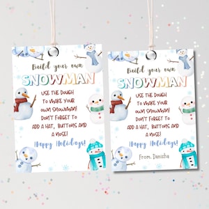 May include: Two rectangular gift tags with a snowman theme. The tags feature the text "Build your own SNOWMAN" and instructions to add a hat, buttons, and a nose. The tags also include the phrase "Happy Holidays!"