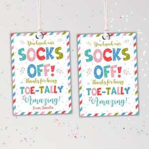 May include: Two rectangular gift tags with the text "You knock our SOCKS OFF! Thanks for being TOE-TALLY Amazing! From: Danisha." The tags have a white background with colorful text and a striped border.