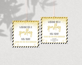 May include: Two square gift tags with the text "Wishing you a sparkling New Year!" in gold script. The tags have a gold glitter border and a black and white striped border. White string is attached.