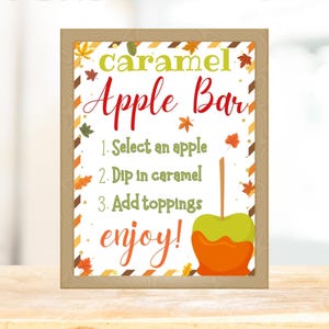 May include: A framed sign with the words "caramel Apple Bar" in green and red, with instructions and an illustration of a caramel apple. The sign has a wooden frame and autumn leaf accents.