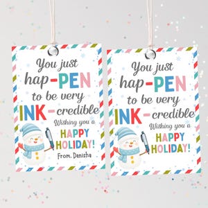 May include: Two rectangular gift tags with a festive design. Each tag features the text "You just hap-PEN to be very INK-credible" and "Wishing you a HAPPY HOLIDAY!" A snowman illustration and a pen are also included.