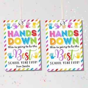 May include: Two rectangular gift tags with white string. The tags have a white background with colorful handprints and a rainbow border. Text on the tags reads "HANDS DOWN this is going to be the Best SCHOOL YEAR EVER!" and "From: Danisha."