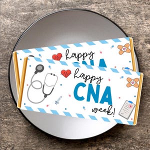 May include: Two candy bar wrappers with a blue and white design, featuring medical icons and the text "Happy CNA week!". The wrappers are on a gray plate, set against a textured, neutral background.