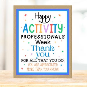 May include: A framed sign with a light brown border and a blue inner border. The sign reads "Happy ACTIVITY PROFESSIONALS Week Thank you FOR ALL THAT YOU DO! YOU ARE APPRECIATED MORE THAN YOU KNOW!" in colourful text.