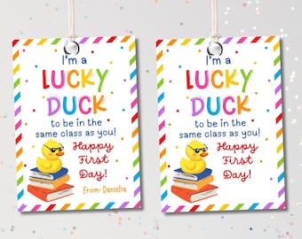 May include: Two rectangular gift tags with a colorful rainbow border and the text "I'm a Lucky Duck to be in the same class as you! Happy First Day!" A yellow duck wearing sunglasses sits atop books.