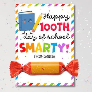 May include: A colorful card with the text "Happy 100th day of school SMARTY!" features a cartoon book and pencil. A wrapped candy is at the bottom. The card has a rainbow border and the name "DANISHA" is printed on the card.