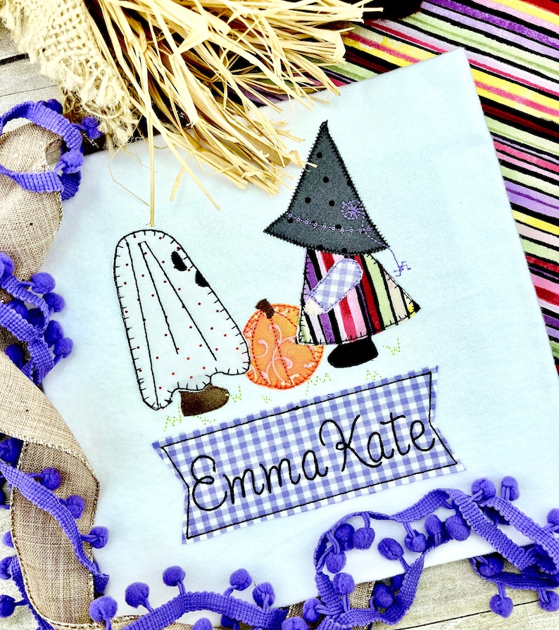 May include: A white onesie with a ghost and witch applique. The witch is holding a pumpkin and the onesie is personalized with the name "Emma Kate".