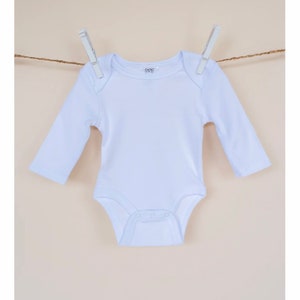 May include: A white long-sleeved baby onesie hanging on a clothesline with two clothespins. The onesie has a small logo on the front that says "6-12M".