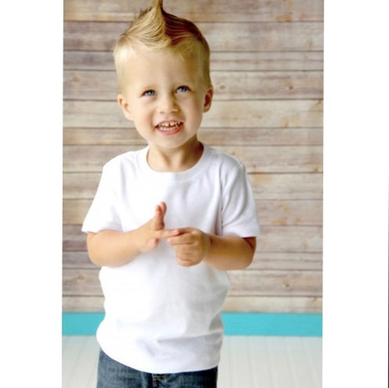 May include: A young boy with a spiky blond hairstyle is wearing a white t-shirt. He is smiling and looking up.