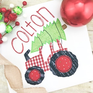 May include: A white fabric with red embroidered text "COLTON" and a red and white checkered tractor pulling a green Christmas tree.